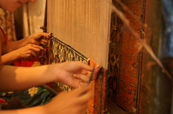 Weavers weaving a small oriental rug with a rug loom
